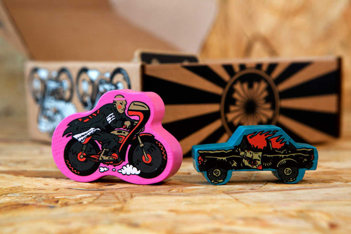 Nahaufnahme der handgefertigten Spielsteine aus massivem Buchenholz, gestaltet in Form eines detailreichen Bōsōzoku-Motorrads und eines klassischen Polizeiautos. Die farbenfrohen, bedruckten Holzfiguren unterstreichen die handwerkliche Qualität und den Retro-Charme des Spiels „Catch Me Aho“. Die Motive greifen die rebellische Bōsōzoku-Kultur auf und verleihen dem Spiel eine besondere visuelle Note.