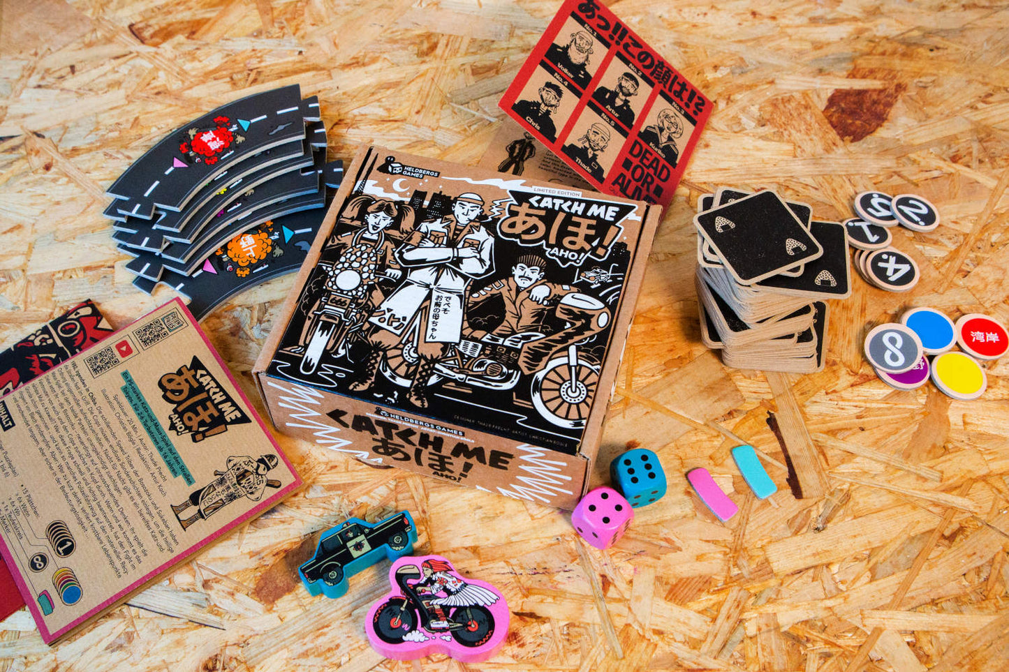 Komplettansicht der aufgebauten Spielkomponenten von „Catch Me Aho“ inklusive Spielkarten, Spielfiguren, Rennstrecke und Verpackung. Die Gestaltung und der Retro-Stil der Box und des Inhalts machen das Spiel zu einem Hingucker und einem Muss für Sammler und Liebhaber der japanischen Straßenkultur. Das Spiel bietet eine einzigartige Kombination aus taktischer Tiefe und einem unverwechselbaren visuellen Stil.