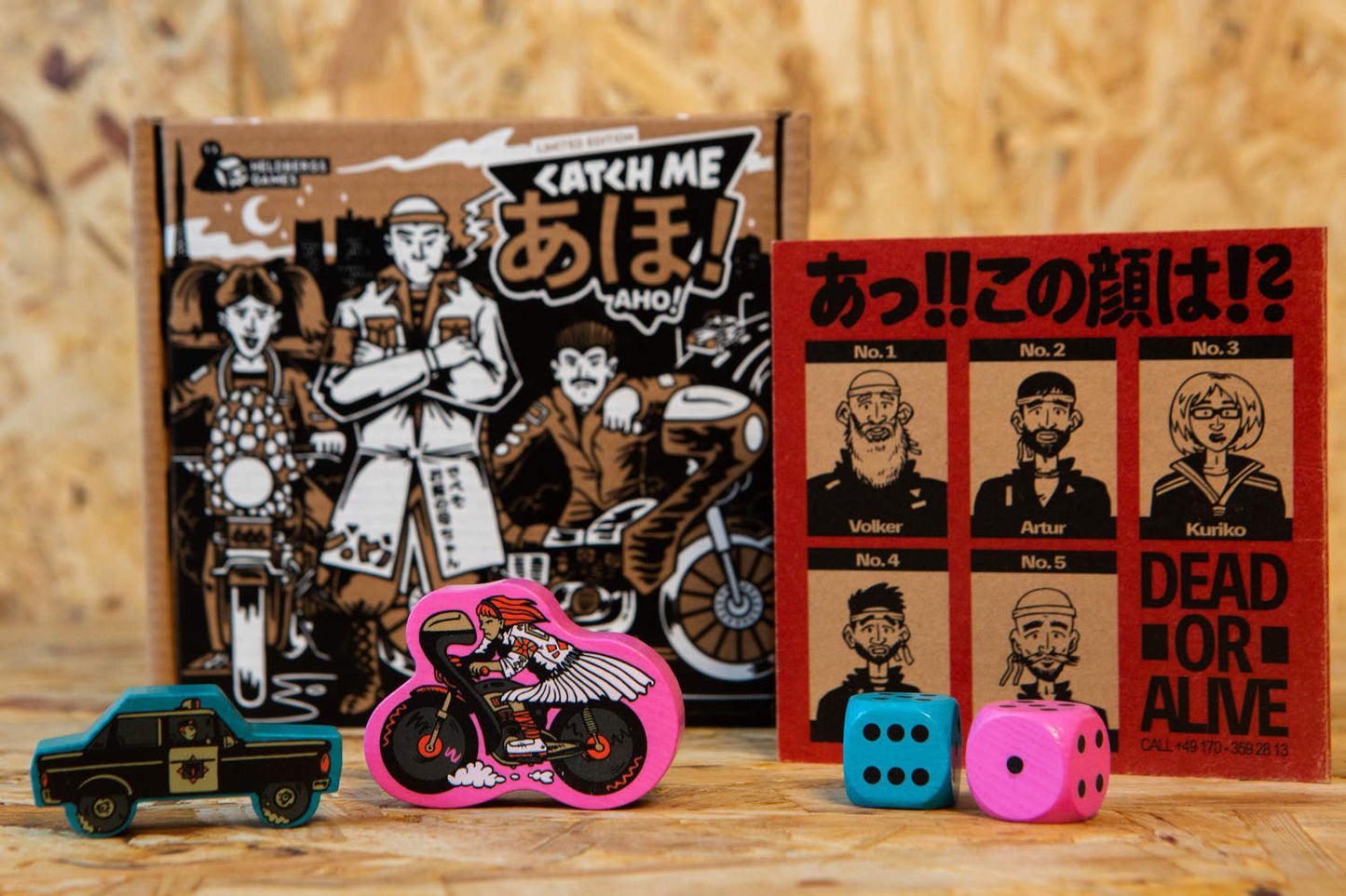 Nahaufnahme der Spielfiguren und eines „Wanted“-Posters aus dem Spiel „Catch Me Aho“. Die Spielfiguren – ein Motorradfahrer und ein Polizeiwagen – sind aus lokalem Buchenholz gefertigt und mit farbenfrohen, markanten Illustrationen bedruckt. Das „Wanted“-Poster fügt eine humorvolle, ironische Note hinzu und verstärkt die Atmosphäre der japanischen Straßenkämpfe in den 1980er-Jahren, die das Spiel einfängt.