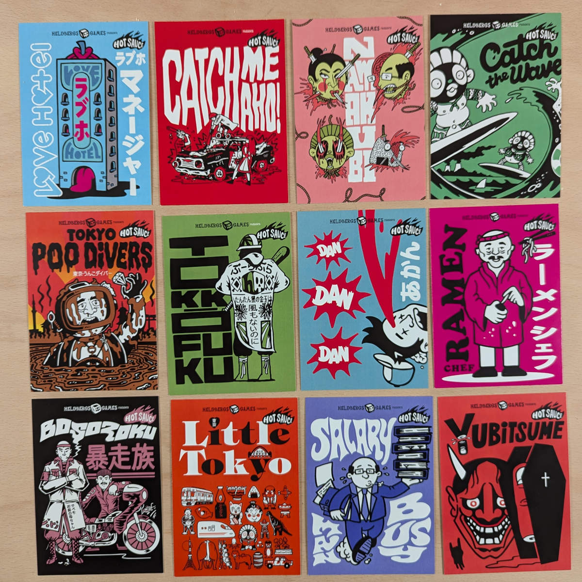 Zwölf Postkarten von Heldbergs Games, organisiert in einem Raster. Verschiedene Themen wie Love Hotel, Bosozoku, Catch the Wave, Ramen Chef. Farbenfrohe, detailreiche Designs inspiriert von japanischer Kultur und Pop-Art.